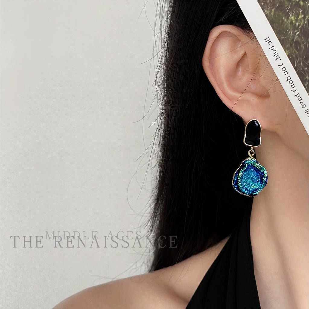 Pair of Blue Tears textured blue druzy earrings held in hand