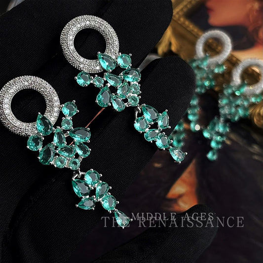 Close up of green zircon chandelier earrings held on black velvet glove